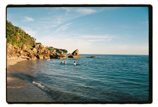 Swimmers in a rocky Mediterranean cove at golden hour