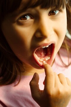 Little girl showing her loose tooth, looking directly into the camera