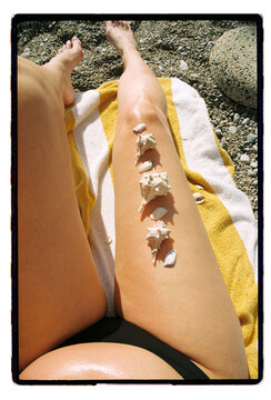 Shells lined up along a tanned leg on a yellow beach towel