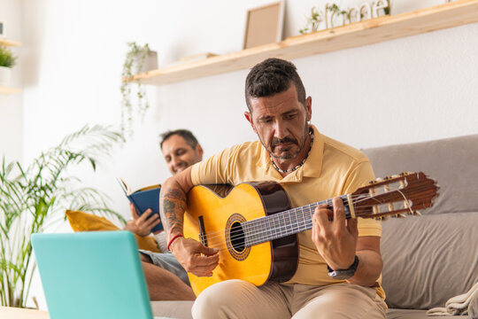 Man learning guitar online with partner reading
