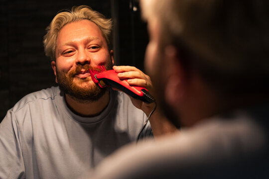 Man Trimming Beard In Front Of Bathroom Mirror