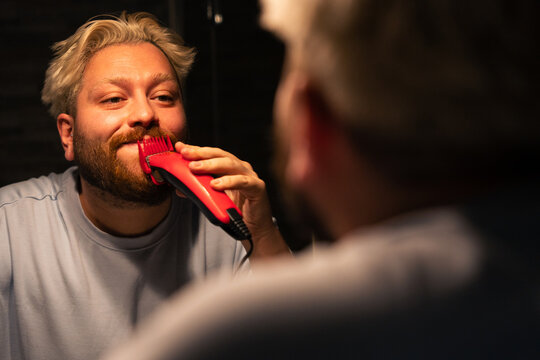 Man Trimming Beard In Front Of Bathroom Mirror