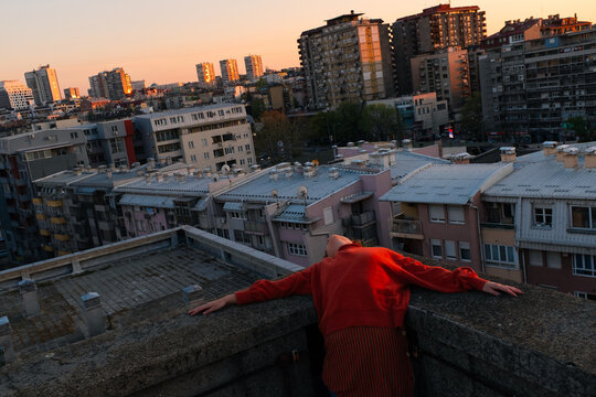 Young Woman Leaning Back On Rooftop Above City At Sunset