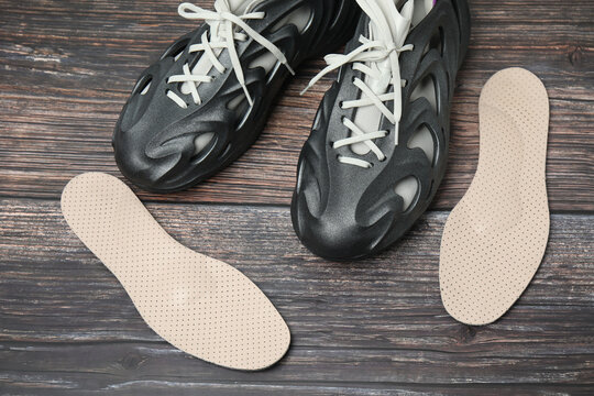 Pair of orthopedic insoles and stylish shoes on the floor
