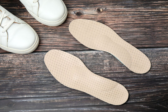 Pair of orthopedic insoles and stylish shoes on the floor
