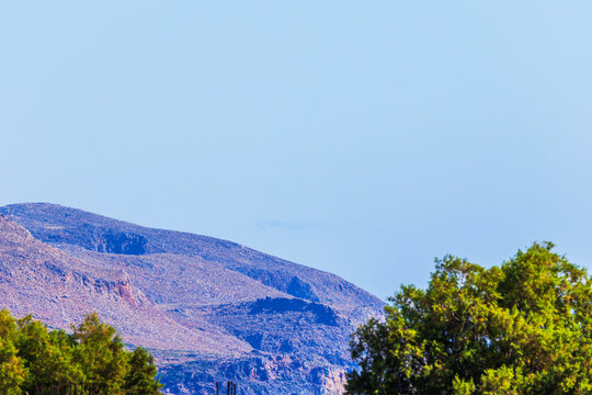 Beautiful view of rocky mountain slope with green trees against clear sky. Crete. Greece.