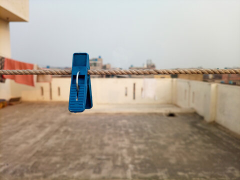 A blue plastic clothes pin or clothes peg for house hanging on rope isolated on roof top, laundry clip, front view