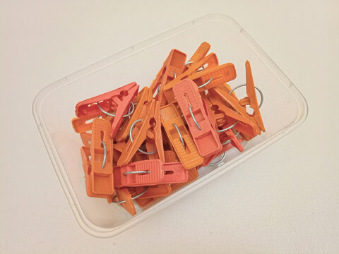 Orange color laundry clips in a container on the white background, multi color sets of plastic clothes pins or clothes pegs for house