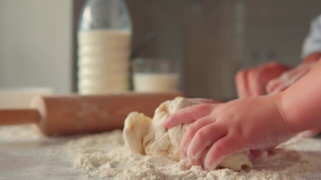 Child's hands learning to knead dough with their mother's help. Close-up of family baking bread together on a kitchen countertop