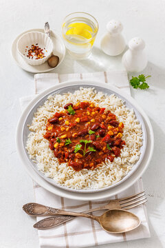 Picadillo Vegetariano con Frijoles with red kidney beans, corn and peppers over steamed white rice served on a plate on light textured table with fork, spoon, vertical, not AI