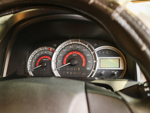 Car dashboard shows speedometer and tachometer. Red needles indicate vehicle operation. Digital display sits beside gauges. Steering wheel frames the instrument panel. Perfect for automotive, travel