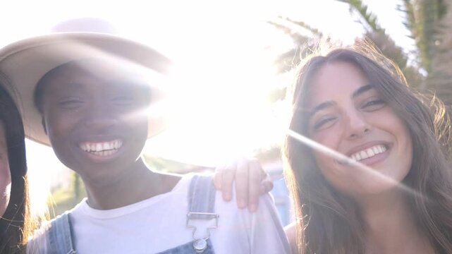 Happy Portrait in slow motion of three multiethnic female friends laughing while embracing each other, outdoors in a beach city, having fun and enjoying of their company.