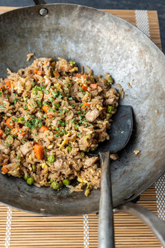 Chicken fried rice in a seasoned carbon steel wok on a dark surface 