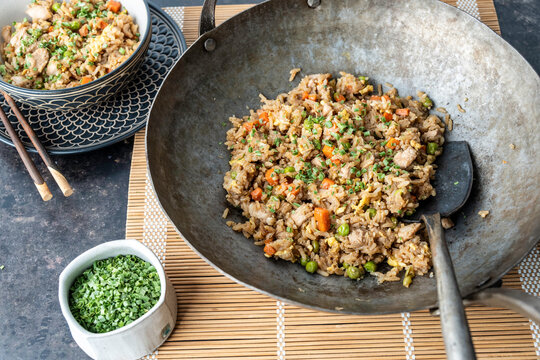 Chicken fried rice in a seasoned carbon steel wok on a dark surface 