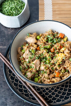 Chicken fried rice with chives in a ceramic bowl on a dark surface 