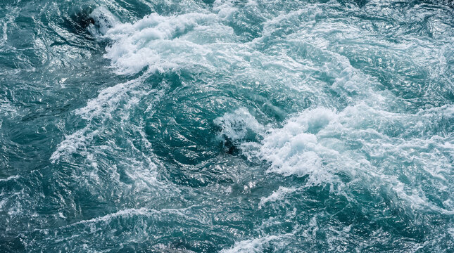 Abstract view of turbulent blue water with powerful rapids, swirling eddies, and white foam, evoking a sense of natural force.