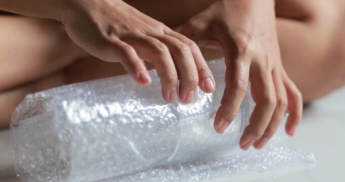 Hands wrapping a clear glass with bubble wrap for safe packaging and shipping, product protection, careful handling, packing, and delivery preparation