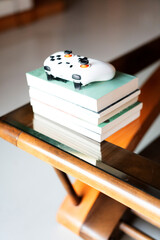 White Xbox controller resting on a stack of books atop a wooden table with glass top — cozy indoor © chuangxin