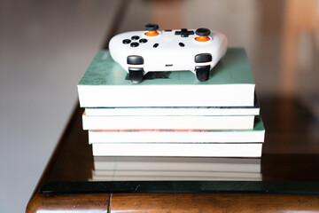 White Xbox controller resting on a stack of books atop a wooden table with glass top — cozy indoor © chuangxin