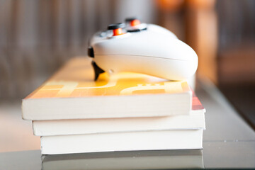 White Xbox controller resting on a stack of books on a glass table in a modern indoor setting © chuangxin