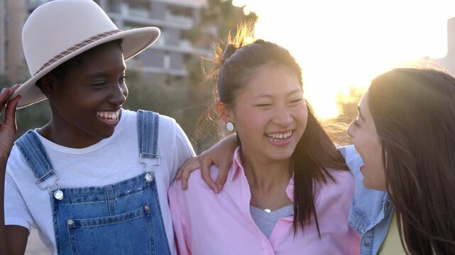 Portrait of three multiracial female friends outdoors looking at each other happily and embracing. Empowered women and equality concept.