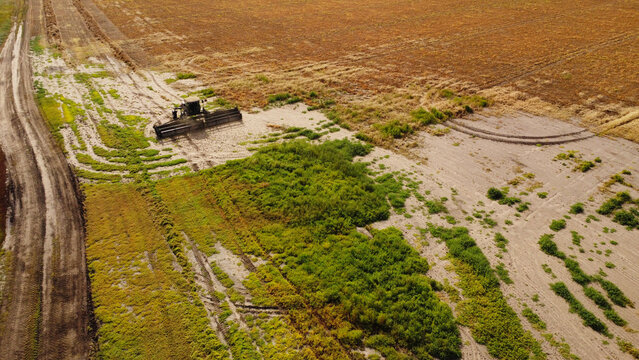 A high-angle drone photograph capturing a self-propelled windrower swather from directly above as it cuts through dense green vegetation in a field.