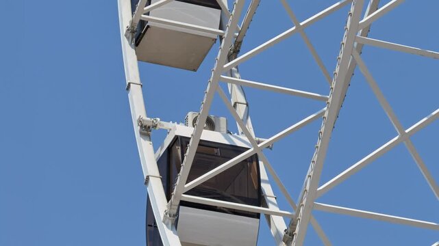 White Ferris wheel rotates gently under cloudless blue sky