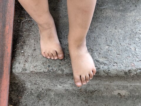 Barefoot child feet standing on a rough concrete surface outdoors, top view showing toes, toenails and natural foot position.