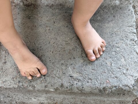Barefoot child feet standing on a rough concrete surface outdoors, top view showing toes, toenails and natural foot position.
