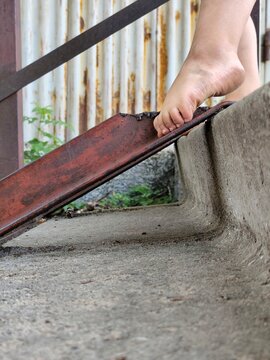 Barefoot child feet stepping on a rusty metal beam beside a concrete surface outdoors, close view of toes, heel and foot position while walking.

