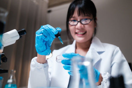 Scientist pipetting blue liquid into petri dish in laboratory