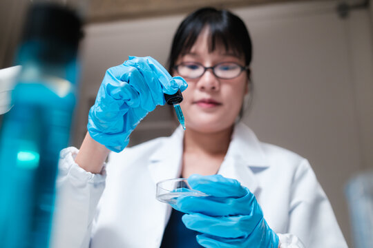 Asian scientist dripping liquid into petri dish in lab
