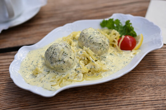 Pike meatballs in dill sauce served on mashed potatoes pressed into noodle shapes, served with salad garnish on a white plate on a rustic wooden table, selected focus
