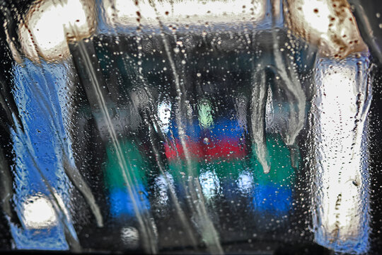 Soap and water running on the windshield when driving through a car wash with colorful rotating brushes, abstract blurry background for cleaning service and transportation, copy space