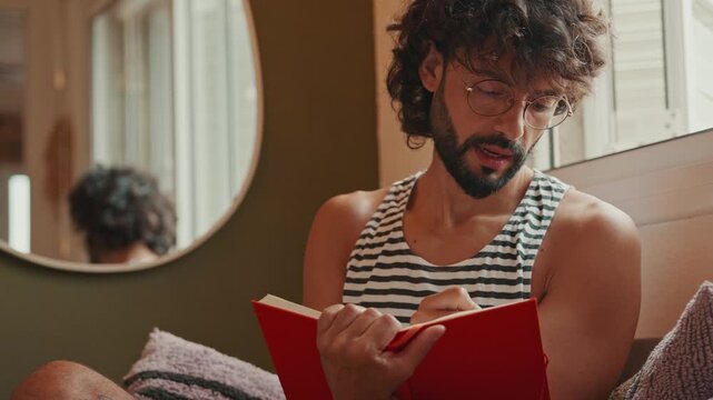 Thoughtful Young Man Writing in a Red Notebook at Home