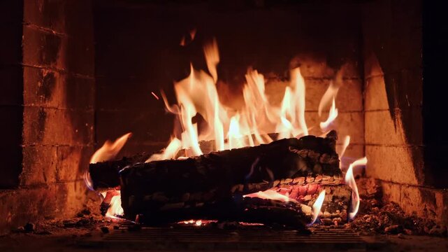 Burning wooden logs with flames and hot glowing embers inside a home fireplace. Cozy winter atmosphere and warm fire indoors.