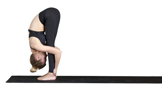 Young woman performing standing forward fold yoga pose while stretching barefoot on an exercise mat