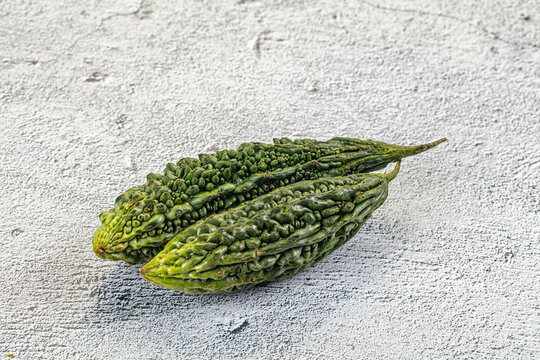 Two green bitter melons on textured white surface