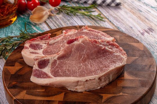 Raw pork chops on wooden cutting board with rosemary garlic and cherry tomatoes