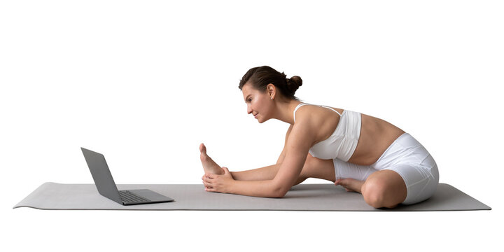 Young woman following an online yoga class while performing a seated hamstring stretch on a mat