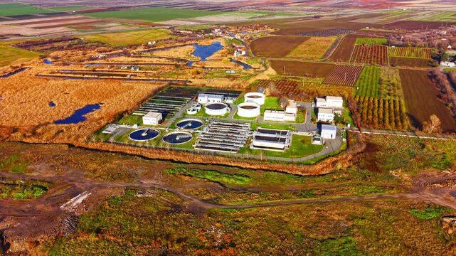 Aerial view of wastewater treatment plant amid farmland. Circular clarifier and wetland canal surround the facility under soft daylight near autumn field.