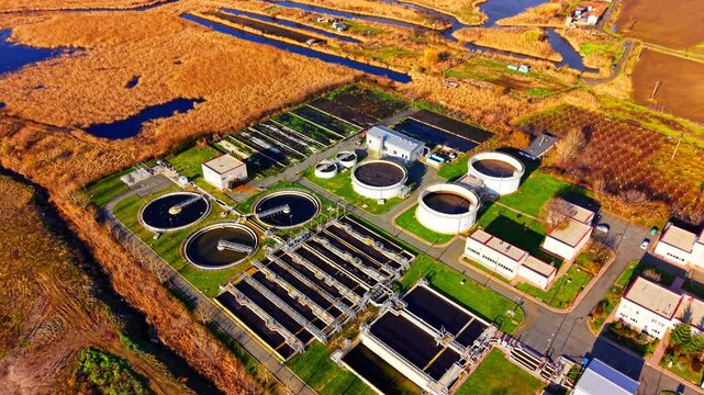 Overhead view of sewage treatment tank near wetland reed. Golden marshland, circular basin and small residential building line the water channel.