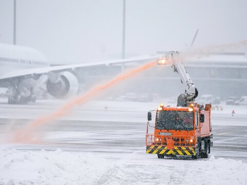 Aircraft de-icing truck sprays fluid on jet wing during snow at airport