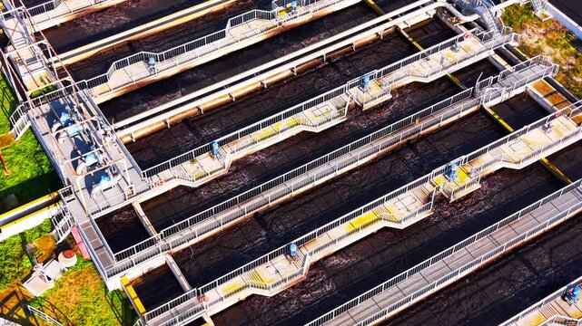 Overhead view of wastewater aeration channel. Diagonal row of dark water basin with metal catwalk and blue valve stretch across a treatment facility.