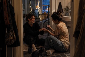 Obraz premium Two woman friends sitting on bathroom floor painting nails during New Year celebration. Happy girls having fun at home during festive winter holiday. Female friendship and care concept.