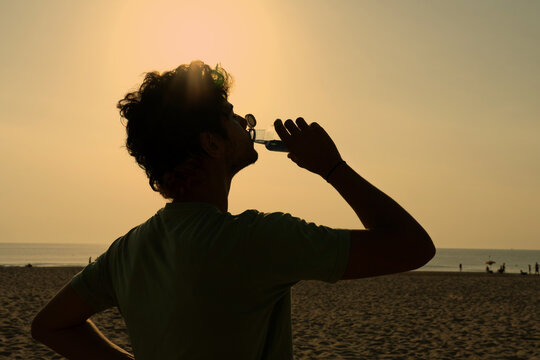 Silhouette of a young man drinking water on the beach at sunset