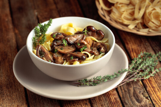 Noodles with mushrooms and thyme on a rustic wooden table.
