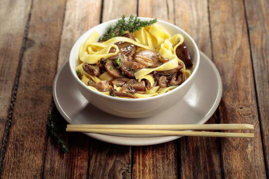Shimeji and shiitake mushrooms stir-fried with soy sauce, garlic and thyme, served with noodles in a ceramic bowl.