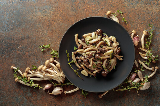 Fried shimeji mushrooms with thyme and garlic on a black plate.