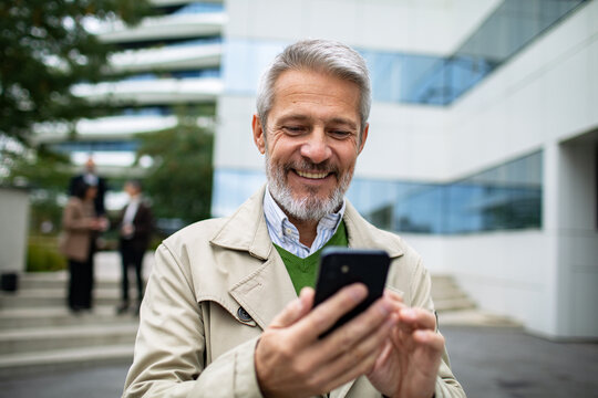 Smiling mature businessman using smartphone outside office